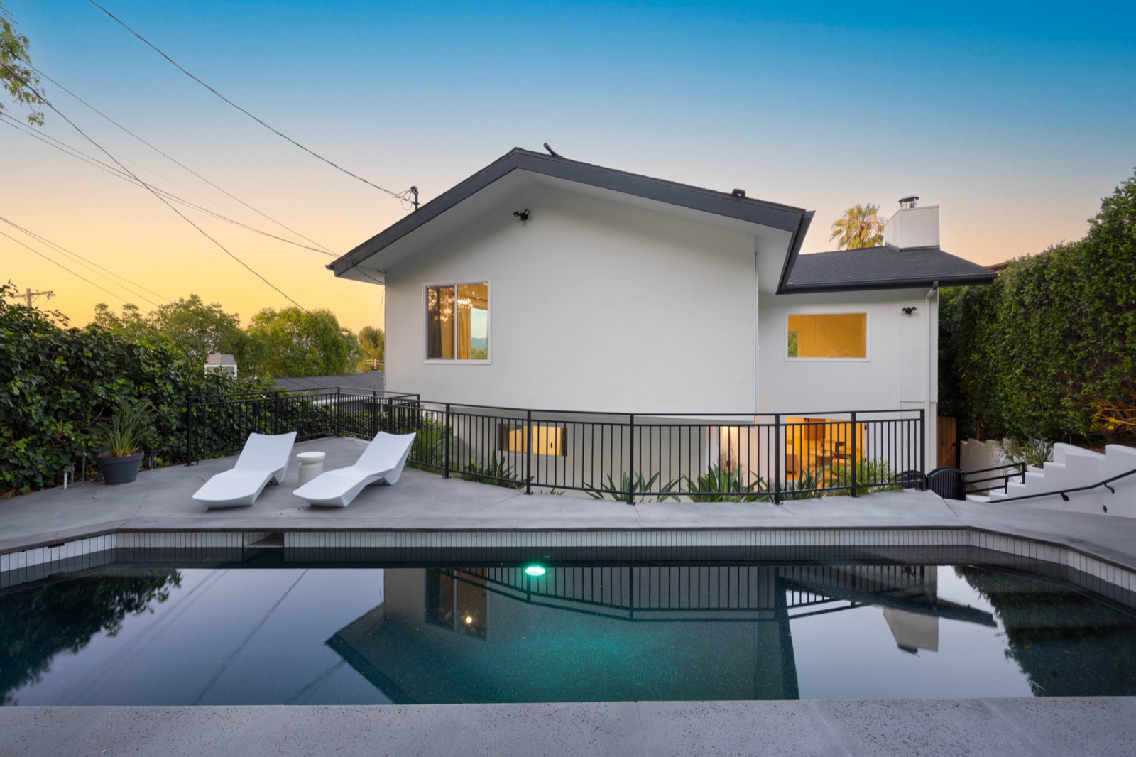 4041 Davana Road in Sherman Oaks at dusk, a white two-story home behind its pool with the Valley lights beyond